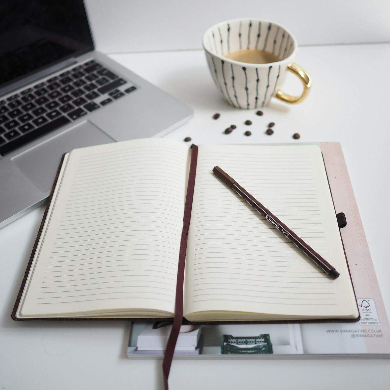 A notebook and laptop on a desk, reviewing notes with a cup of coffee